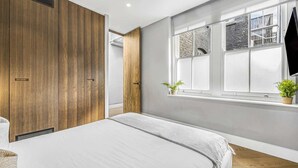 Une chambre à coucher avec un lit, une armoire en bois et une fenêtre ornée de plantes.