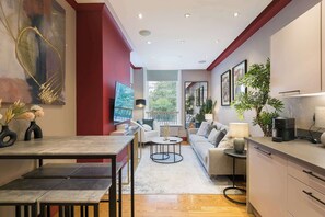 A modern living room with a dining area, a sofa, a coffee table, and a kitchen area with a counter and cabinets. - The Bloomsbury - by Frankie (London)
