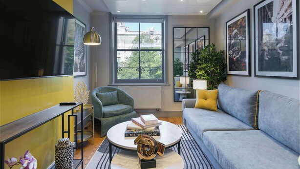 A modern living room with a sofa, armchair, coffee table, and a TV mounted on the wall. - The Bloomsbury - by Frankie (London)