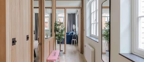 A corridor with wooden doors, a pink bench, a mirror, and a view of a blue sofa and curtains.