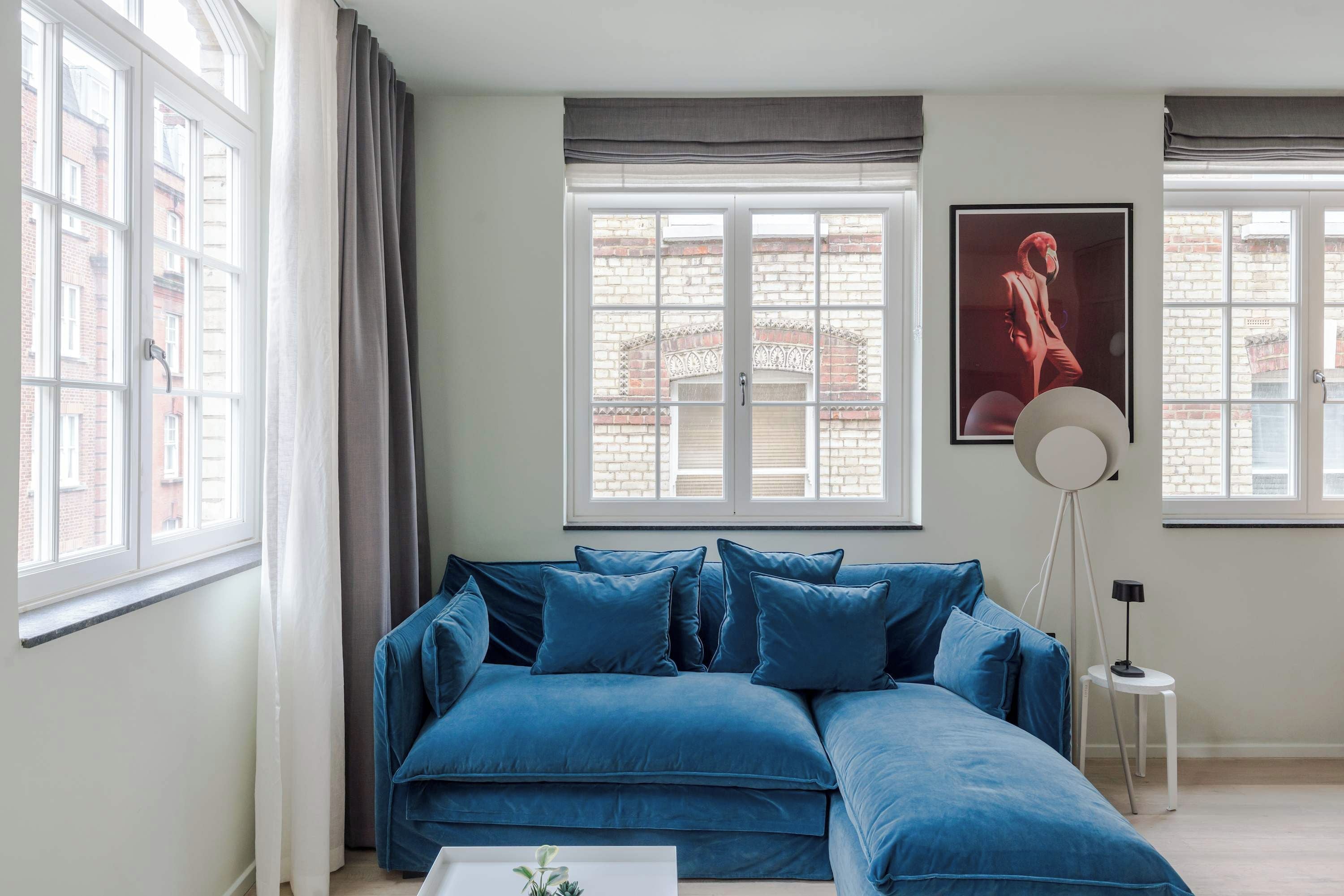 Een kamer met een blauwe hoekbank, een witte salontafel en een vloerlamp.