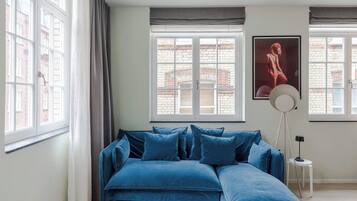 Een kamer met een blauwe hoekbank, een witte salontafel en een vloerlamp.