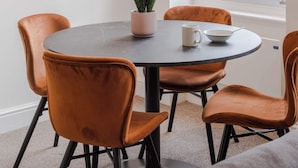 A dining area with a round table, four orange chairs, a framed zebra artwork, a potted plant, and a window with a view of buildings. - The Foley Residence - Fitzrovia - by Frankie (London)