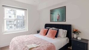 A bedroom with a bed, pillows, a bedside table, a window, and a framed picture on the wall. - The Foley Residence - Fitzrovia - by Frankie (London)