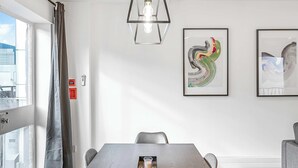 A modern dining area with a long table, chairs, a pendant light, and framed artwork on the walls. - Lumina House - Fitzrovia - by Frankie (London)