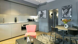 Una cocina moderna con electrodomésticos integrados, un comedor con una mesa redonda y sillas, y una silla rosa.