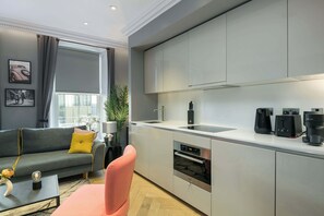 A modern kitchen with built-in appliances, a grey sofa, and a coffee machine. - The Chambers - Covent Garden - by Frankie (London)
