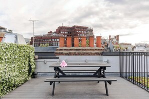 A rooftop terrace with a bench, a potted plant, and a view of buildings in the background. - The Influencer Suite - Soho - by Frankie Says (London)