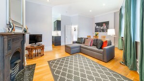 Ein modernes Wohnzimmer mit Kamin, einem grauen Ecksofa und einem Essbereich.