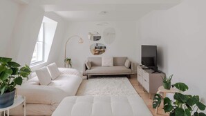 Una sala de estar moderna y bien iluminada con un sofá, una mesita de centro, un televisor y un amplio ventanal que ofrece luz natural.