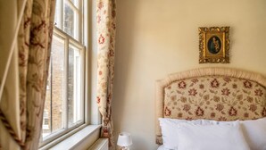 Ein Hotelzimmer mit einem Bett, einem Nachttisch mit Lampe, einem Fenster mit Vorhängen und einem Bilderrahmen an der Wand.