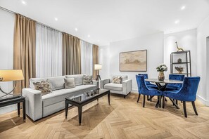A modern living room with a sofa, armchairs, a coffee table, and a dining area with chairs and a table. - Fitzroy Garden - Fitzrovia - by Frankie (London)