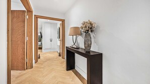A hallway with a wooden door, a dark console table with a lamp and vase, and a herringbone floor. - Fitzroy Garden - Fitzrovia - by Frankie (London)