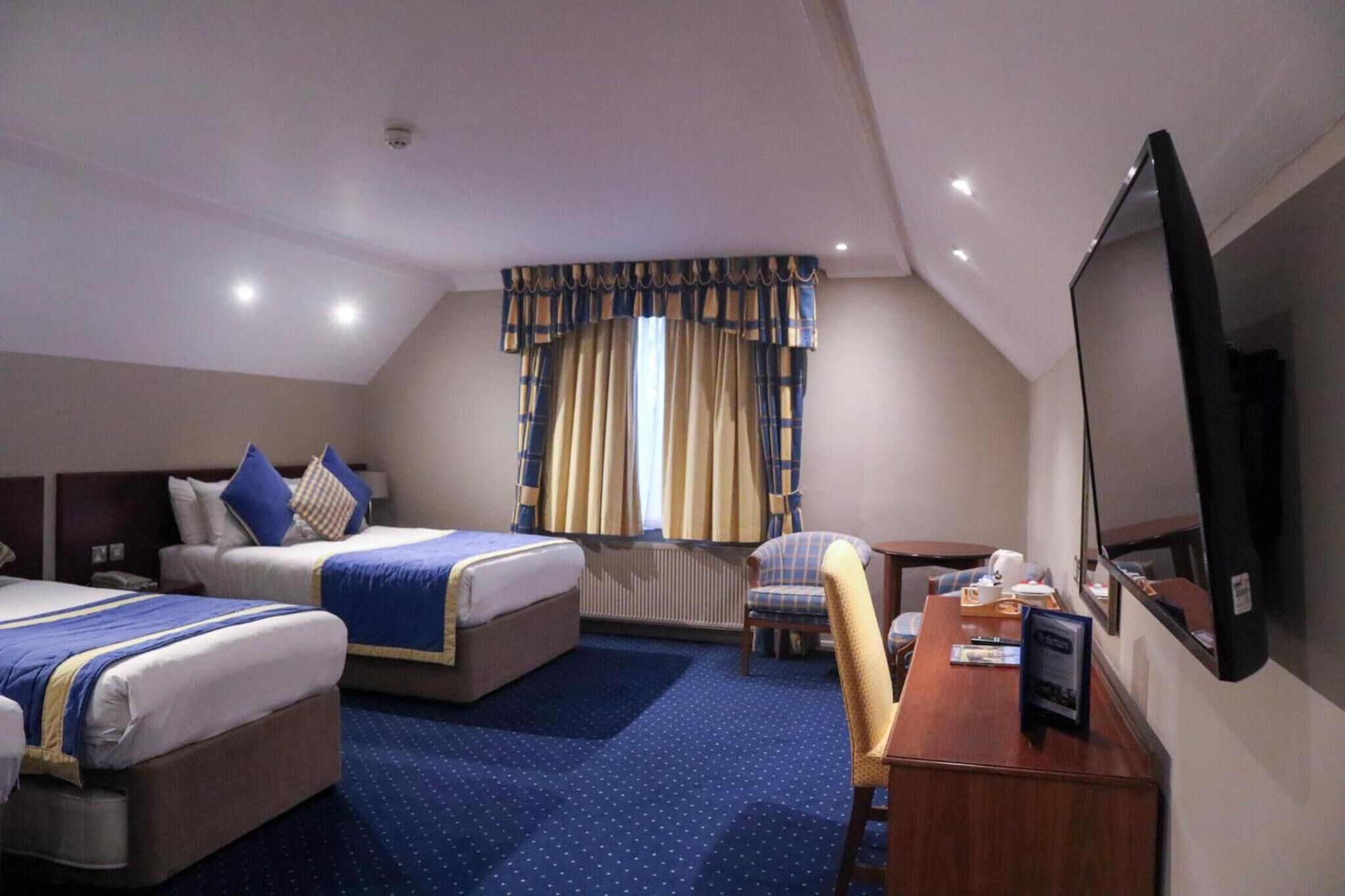 A hotel room with two beds, a desk, a chair, a television, and a window with curtains.