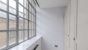 A narrow hallway with a radiator, a window with a view of a brick building, and a set of white doors. - The Eyre Suite Two - Farringdon - by Frankie (London)