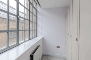 A narrow hallway with a radiator, a window with a view of a brick building, and a set of white doors. - The Eyre Suite Two - Farringdon - by Frankie (London)