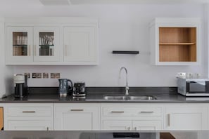 A modern kitchen with white cabinets, a stainless steel sink, a coffee maker, a kettle, and a microwave. - The Eyre Suite Two - Farringdon - by Frankie (London)
