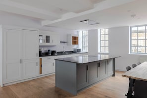 Une cuisine moderne avec des meubles blancs, un îlot central et un coin repas doté d’une table en bois.