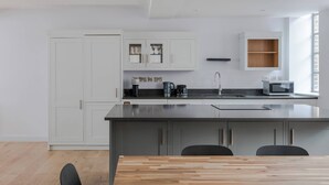A modern kitchen with white cabinets, a central island, and a dining area with a wooden table. - The Eyre Suite Two - Farringdon - by Frankie (London)