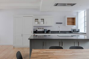 A modern kitchen with white cabinets, a central island, and a dining area with a wooden table. - The Eyre Suite Two - Farringdon - by Frankie (London)