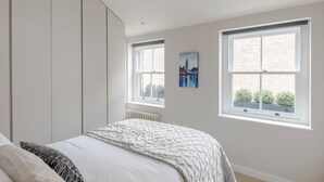 A bedroom with a bed, a radiator, two windows, and a painting of a cityscape. - The Tranquil Den - Regent's Park - by Frankie Says (London)
