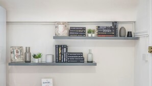 A bookshelf with books and decorative items, a small table with a sign, and a remote control. - The Cutesy - Fitzrovia - by Frankie Says (London)