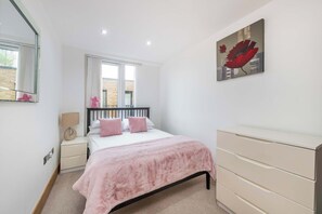 Een slaapkamer met een bed, nachtkastjes, een kaptafel, een raam en een schilderij aan de muur.