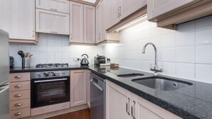 Una cucina moderna con mobili chiari in legno, un piano di lavoro in granito nero, elettrodomestici in acciaio inossidabile e una parete backsplash rivestita di piastrelle bianche.
