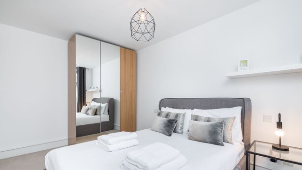 Una camera da letto moderna con un letto grande, un comodino, una lampada a sospensione geometrica e un armadio con specchio.