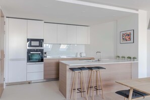 A modern kitchen with white cabinets, a microwave, an oven, a sink, and a bar stool area. - Hollen at Six - Soho - by Frankie (London)