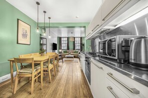 A modern kitchen with a dining area, wooden flooring, and a green wall. - City Ember Fitzrovia by Frankie (London)