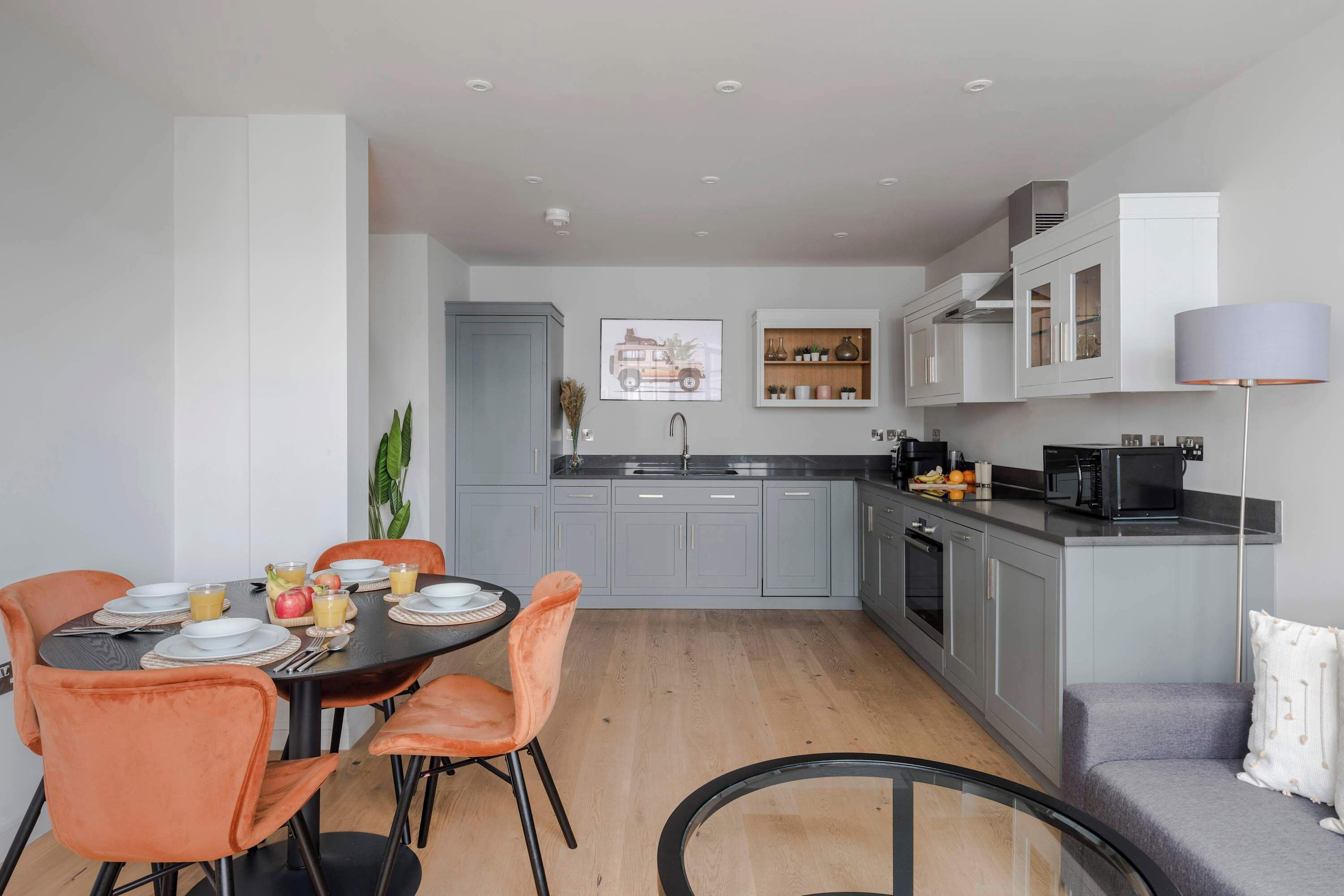 Una cocina moderna con armarios grises, una mesa de comedor con sillas anaranjadas y un sofá gris.