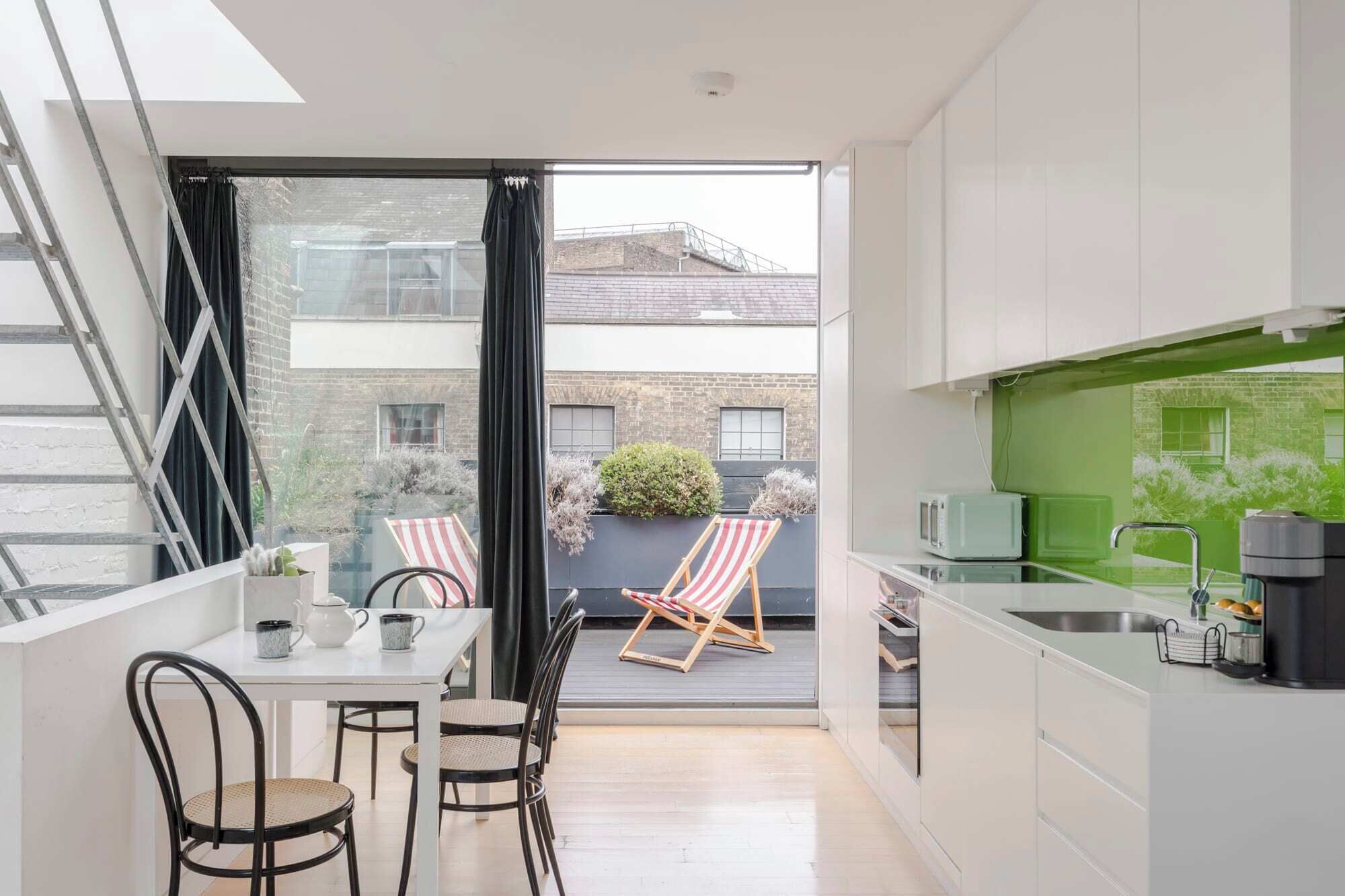 Een moderne keuken met witte kasten, een groene spatwand en uitzicht op de stad door grote ramen.