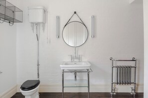 A bathroom with a white toilet, a white sink with a glass shelf, a mirror, a towel rack, and a radiator. - A Starry Starry Night - Borough - by Frankie Says (London)