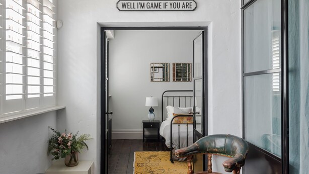 A narrow hallway with a bed, a chair, and a sign reading "WELL I'M GAME IF YOU ARE". - The Dream Factory - Borough - by Frankie Says (London)