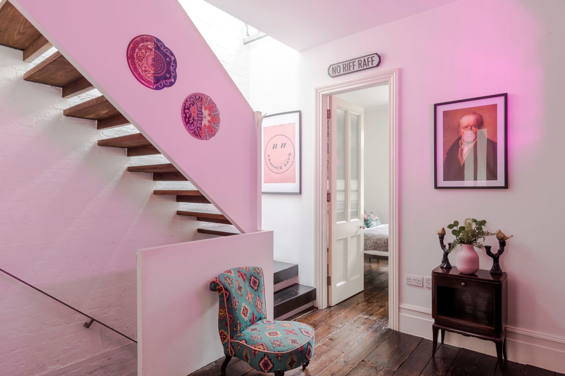 A staircase with a pink wall, a chair, and a small table with decorative items.