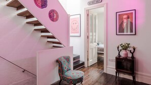 A staircase with a pink wall, a chair, and a small table with decorative items. - The Dream Factory - Borough - by Frankie Says (London)