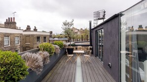A rooftop terrace with wooden flooring, a seating area, and a view of surrounding buildings. - The Dream Factory - Borough - by Frankie Says (London)