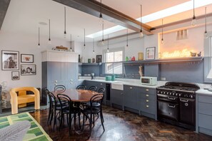 A modern kitchen with a dining area, featuring a large island, a gas stove, and a neon sign. - The Dream Factory - Borough - by Frankie Says (London)