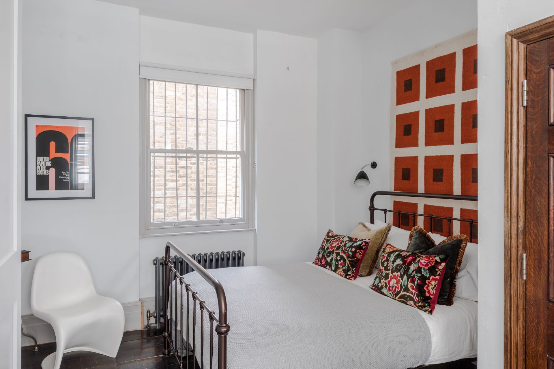 A bedroom with a bed, a radiator, a window, a chair, and a door.