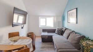 A modern living room with a grey sofa, a wooden dining table, and a TV mounted on the wall. - Wonderland - Fitzrovia - by Frankie Says (London)