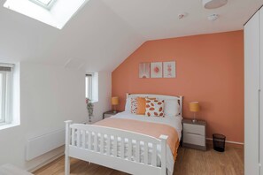 A bedroom with a sloped ceiling, a bed with a white frame, a nightstand, a bedside table, and a window. - Wonderland - Fitzrovia - by Frankie Says (London)