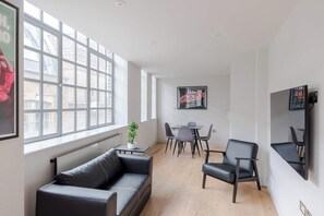 A modern room with a black leather sofa, a dining table with chairs, and a large window with a view of buildings. - The Eyre Suite Four - Farringdon - by Frankie (London)