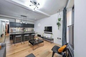 A modern kitchen with a central island, bar stools, a dining table, and a TV mounted on the wall. - The Acre Abode - Covent Garden - by Frankie (London)