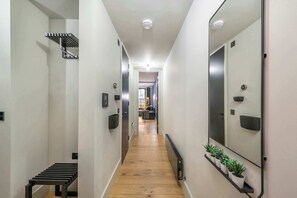 A narrow hallway with a wooden floor, a metal bench, a radiator, and a mirror on the right wall. - The Acre Abode - Covent Garden - by Frankie (London)