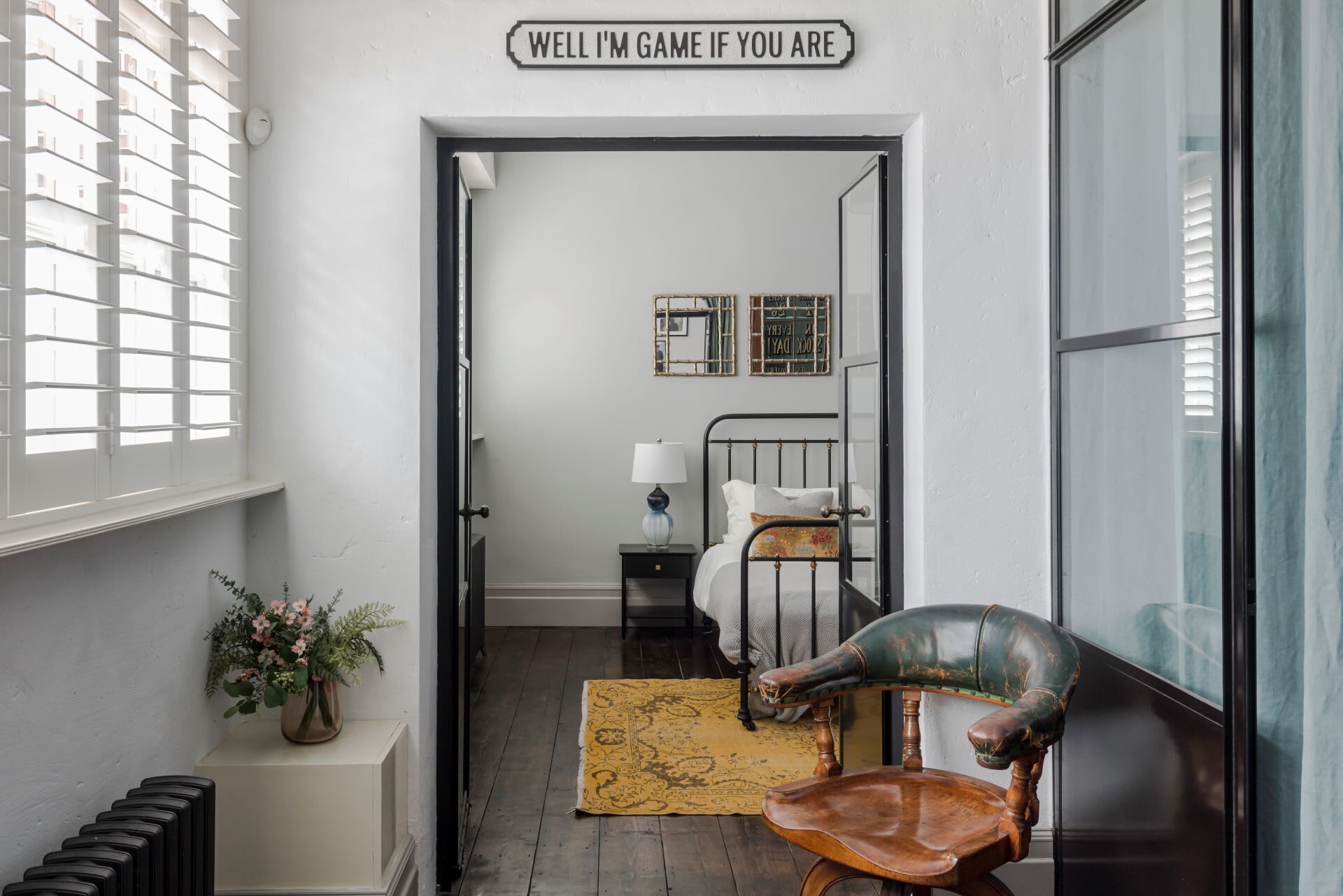 A narrow hallway with a bed, a chair, and a sign reading "WELL I'M GAME IF YOU ARE".