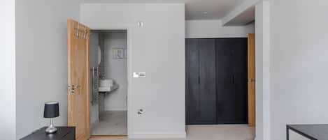 Une chambre à coucher avec un lit, une table de chevet, une lampe, une armoire et une salle de bain visible à travers une porte ouverte.
