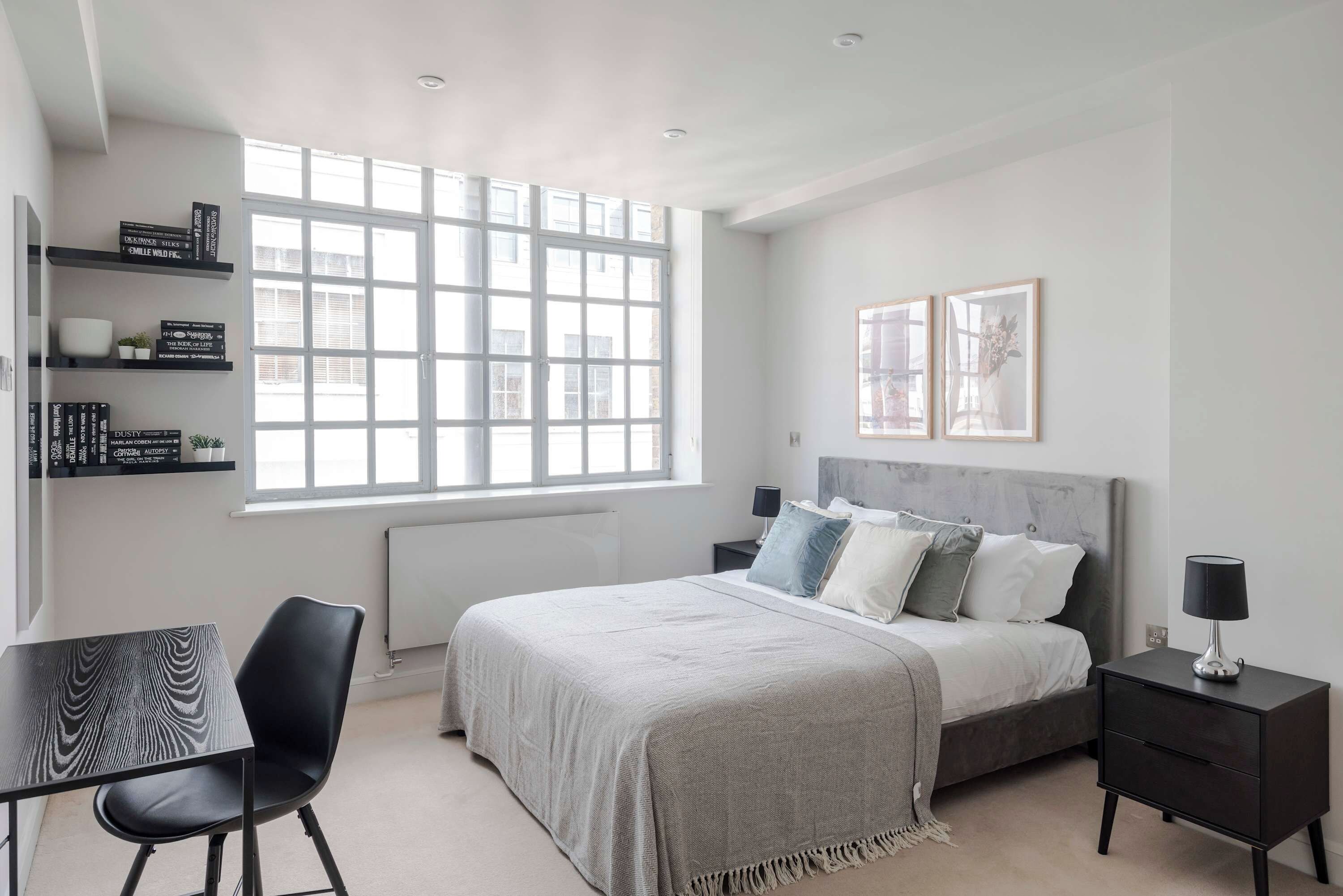 A bedroom with a bed, bedside tables, a chair, a desk, and a window.