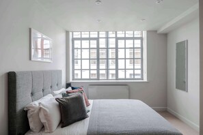 Un dormitorio con cama, ventana, radiador y un cuadro colgado en la pared.