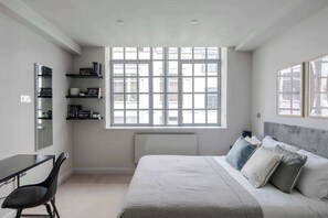 Une chambre à coucher comprenant un lit, un bureau, une chaise, une fenêtre et des étagères intégrées.